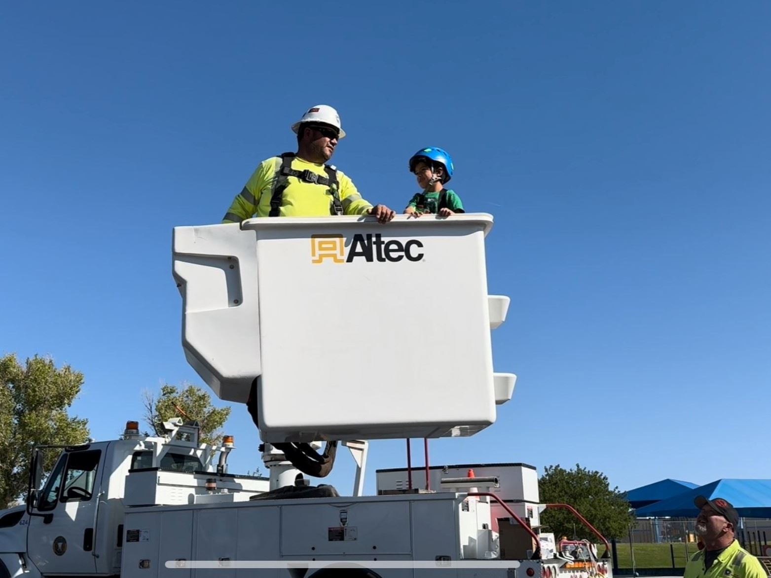 Public Power Week 2024: Electrical worker and elementary school child riding in power truck bucket